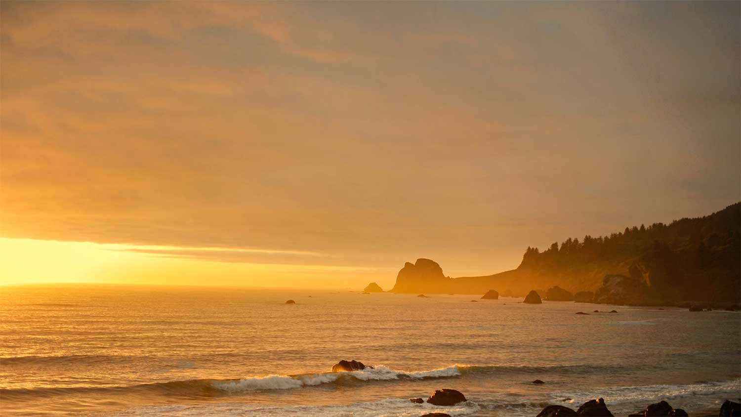 A view of a sunset over the coast, with golden and calm ocean waters.