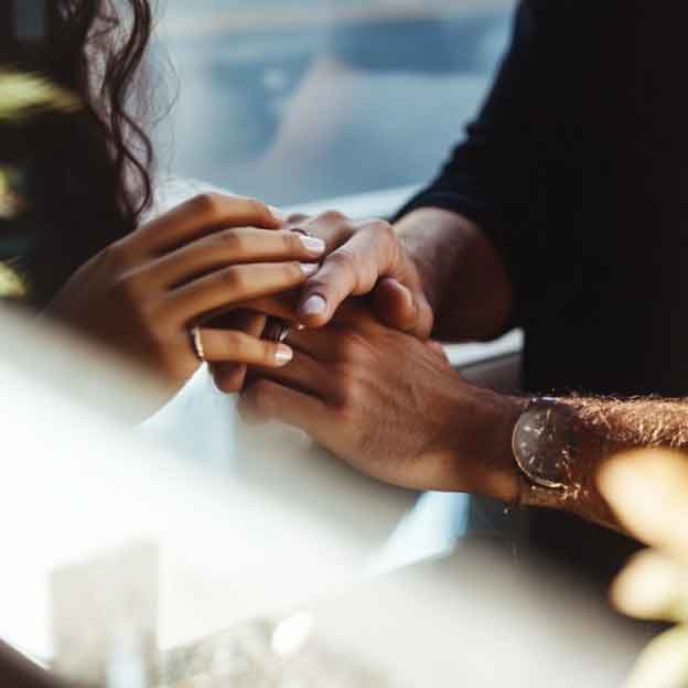Two people holding hands across a table in soft natural light, representing the supportive connection and interpersonal skills practiced in DBT therapy sessions