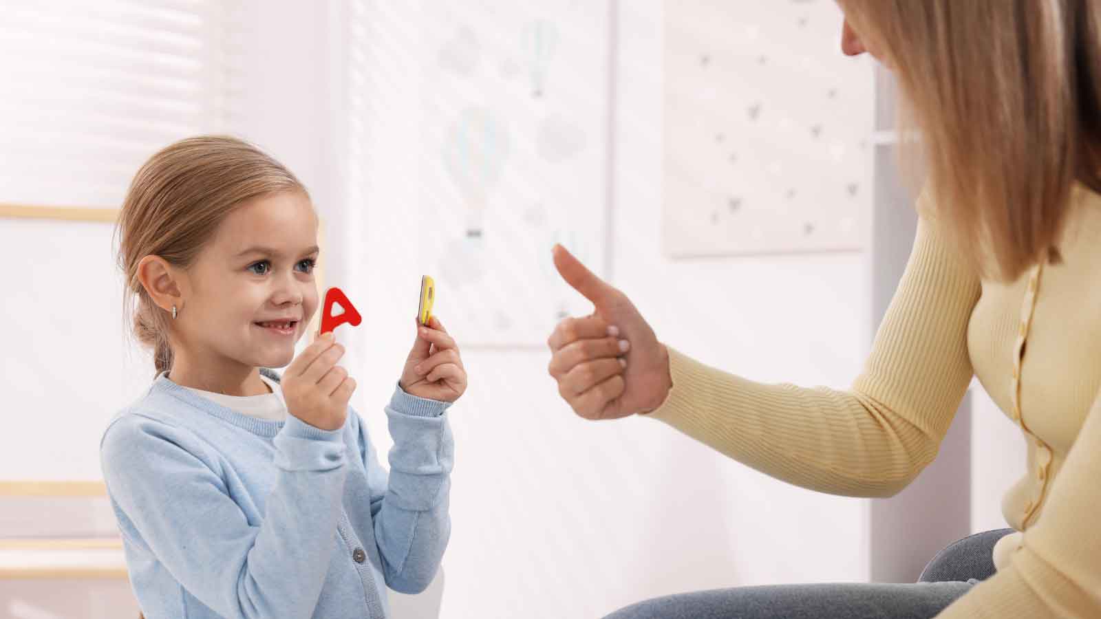 Girl holding alphabet letters while an adult gives a thumbs-up.