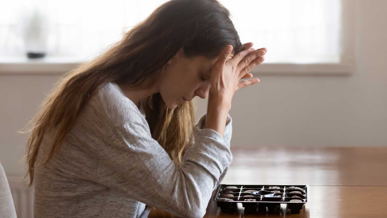 Woman-with-head-in-hands-beside-chocolates Woman with head in hands beside chocolates.