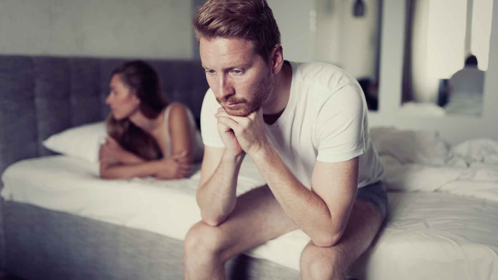 A-man-sitting-on-the-bed,-looking-pensive A man sitting on the bed, looking pensive.