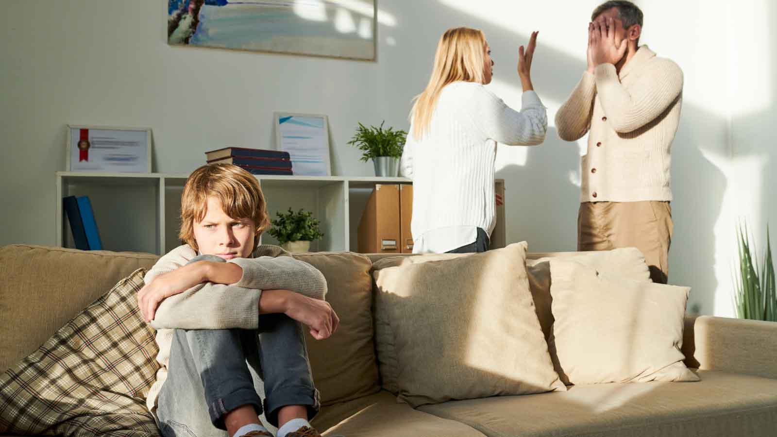 Child-sitting-upset-while-adults-argue-in-background Child sitting upset while adults argue in background