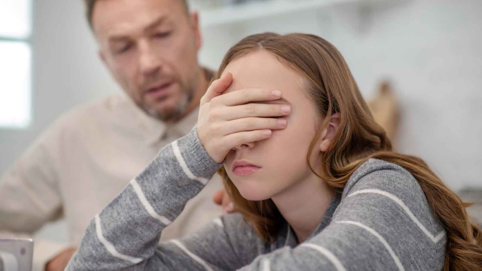 Teen-covering-face-in-frustration-while-adult-looks-on Teen covering face in frustration while adult looks on