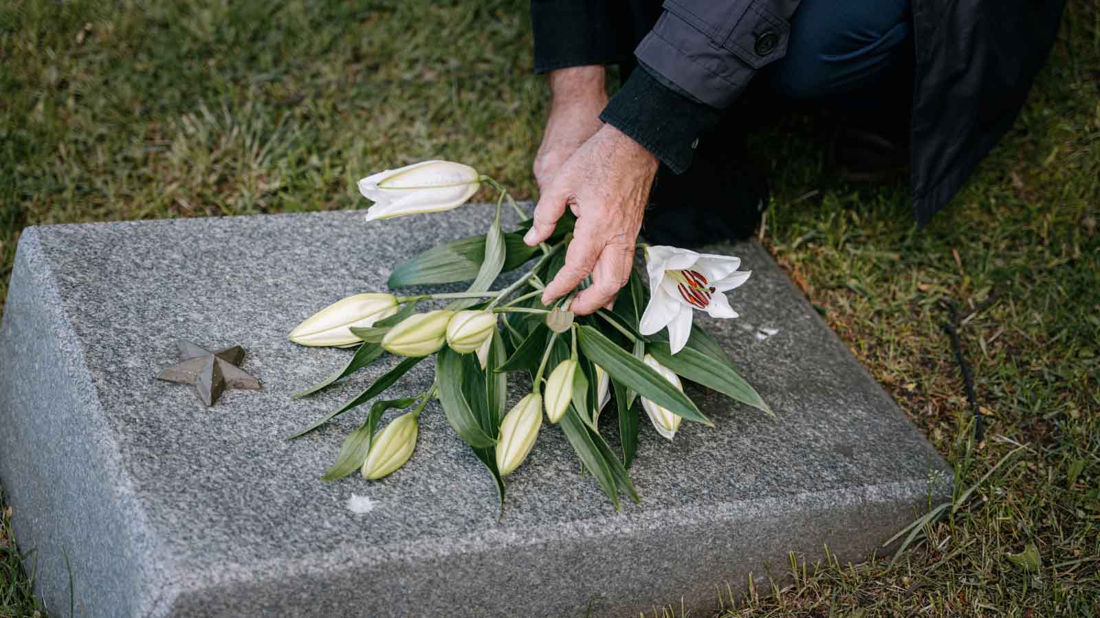A hand placing flowers on a headstone.
