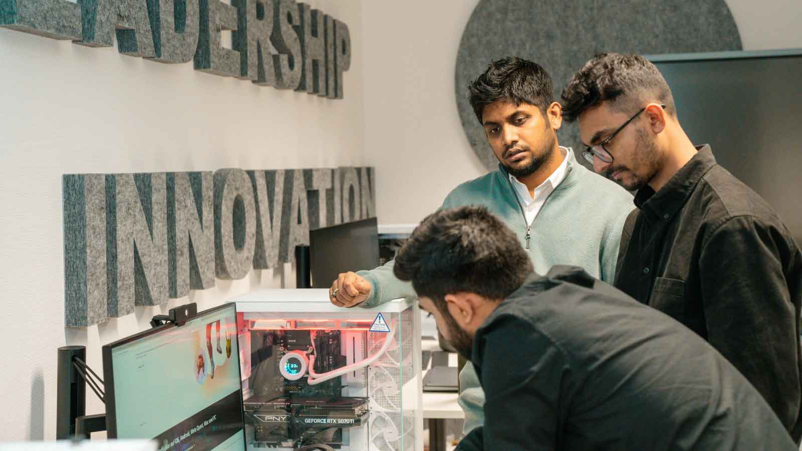 Three-people-examining-a-desktop-computer-setup Three people examining a desktop computer setup.